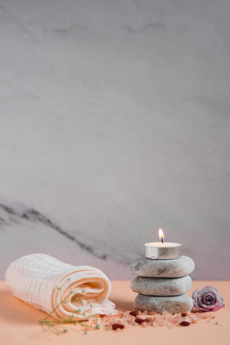 lighted candle spa stones with napkin rose himalayan salts peach colored backdrop against grey background